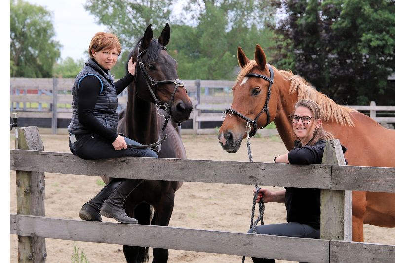 Karen Wouters en Michelle Eugène, oprichters van Horse Academy, naast elkaar met paard, symbool voor hun passie voor paardenwelzijn.